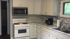A compact kitchen with white cabinets, a stainless steel microwave, a gas stove, and a sink. - Beautiful Cottage on Arbutus Lake, Traverse City, MI 49696 (Traverse City)