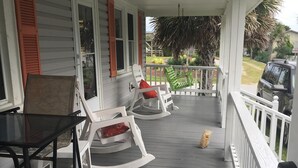 A covered porch with white railings, two rocking chairs with red cushions, a black table, and a dog on the floor. - Come, relax and enjoy all that Atlantic Beach has to offer!!  (Atlantic Beach)