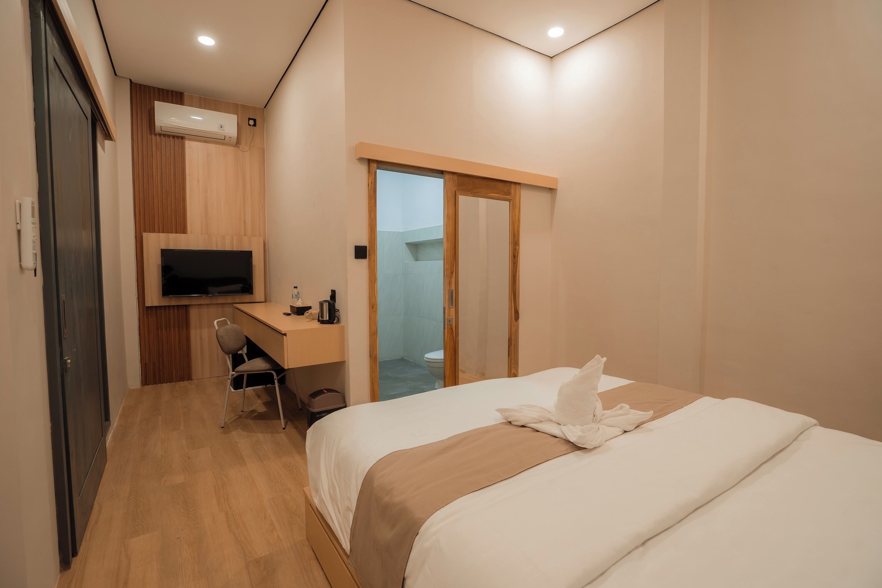 A hotel room with a bed, a desk with a chair, a television, and a bathroom visible through an open door.