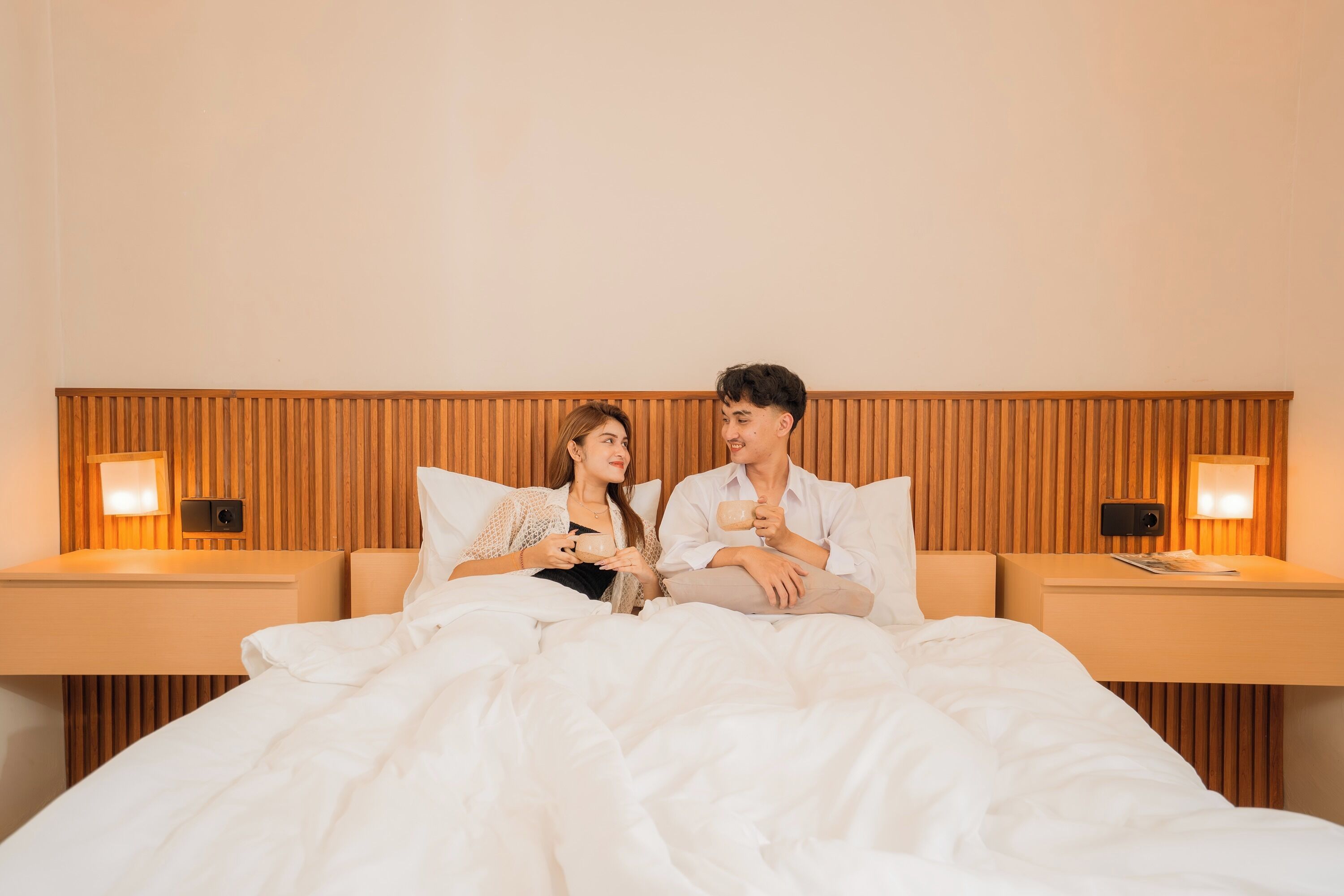 A bedroom with a wooden headboard, two bedside tables with lamps, and a bed with white bedding.