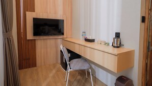 Ein kompaktes Hotelzimmer mit einem Holztisch, einem an der Wand befestigten Fernseher, einem Sessel und einer kleinen Mülleimer.