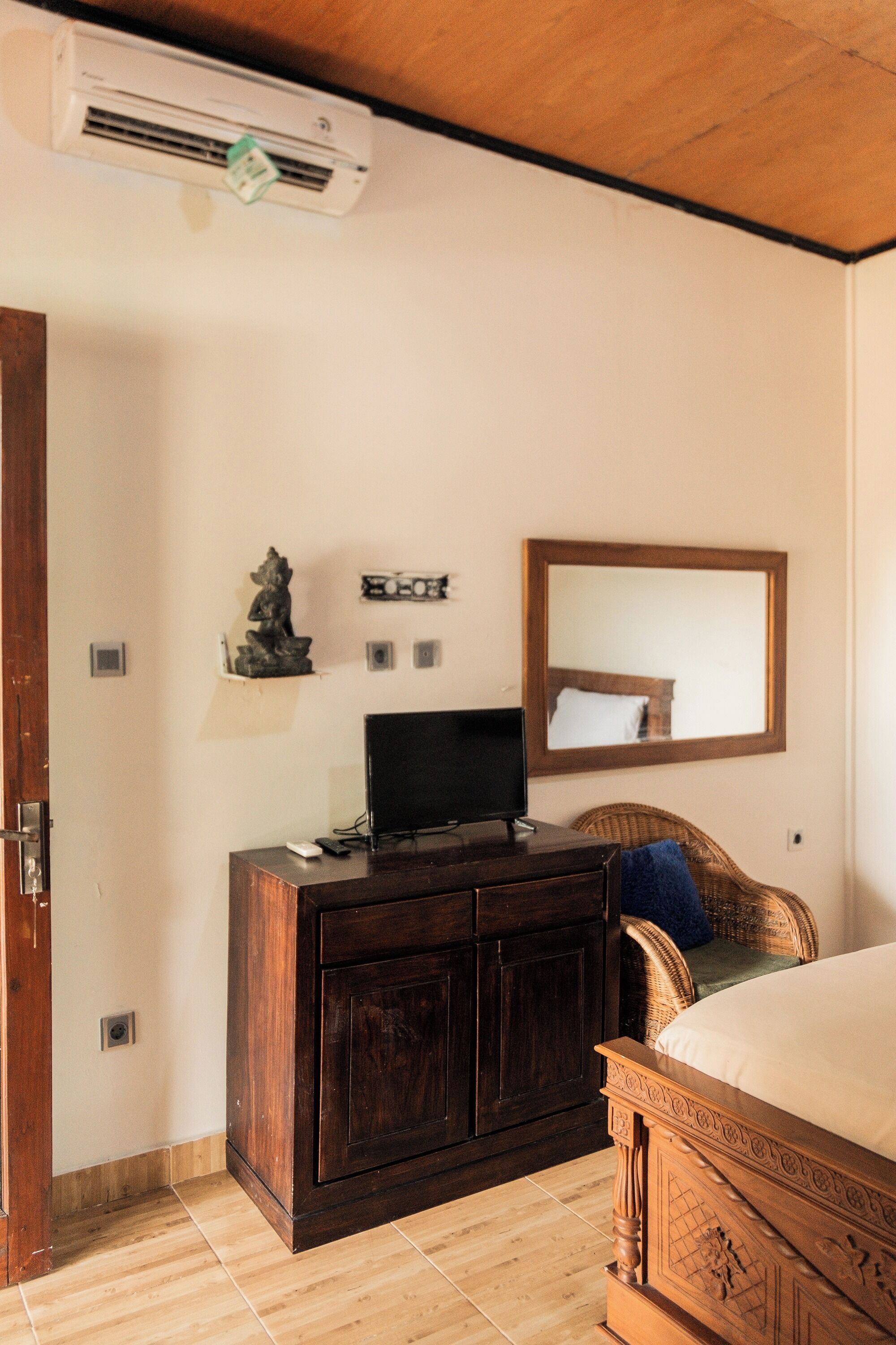 A bedroom with a wooden bed, a dark wooden dresser, a television, and a wall-mounted air conditioner.
