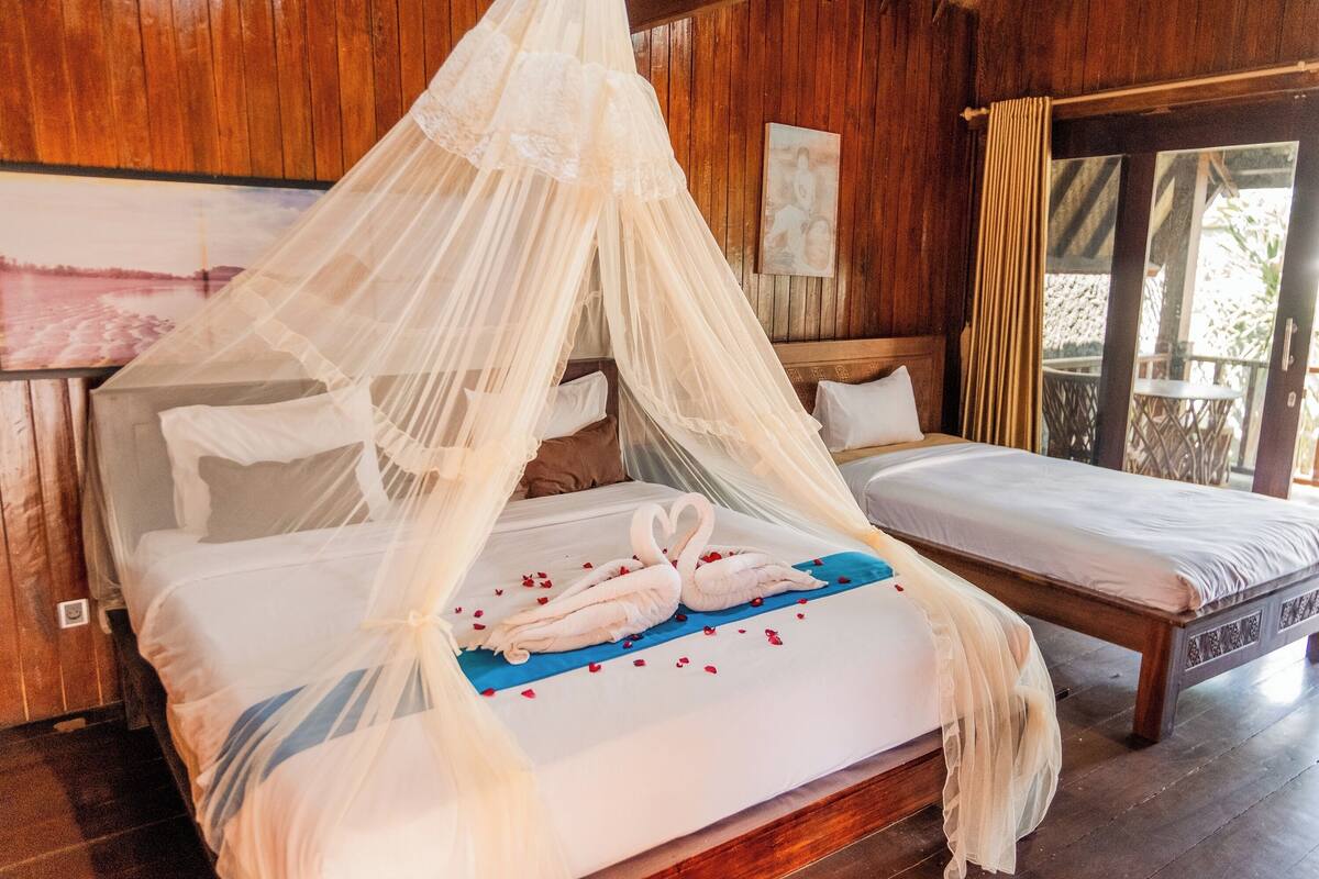 A room with a bed under a canopy, a second bed, wooden walls, and a painting on the wall.