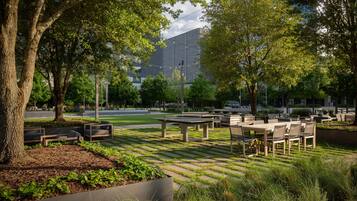 An outdoor seating area with tables and chairs, surrounded by trees and greenery.