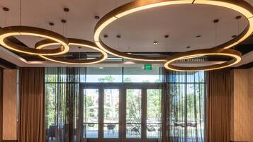 Un hall d’entrée spacieux, doté de grandes portes vitrées, de luminaires circulaires au plafond et d’un tapis à motifs.