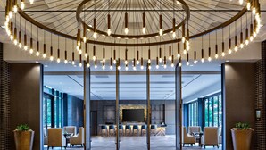 A modern hotel lobby with a circular ceiling light fixture, a large flat-screen TV, and a bar area with bar stools. - Houston Cityplace Marriott at Springwoods Village (Spring)