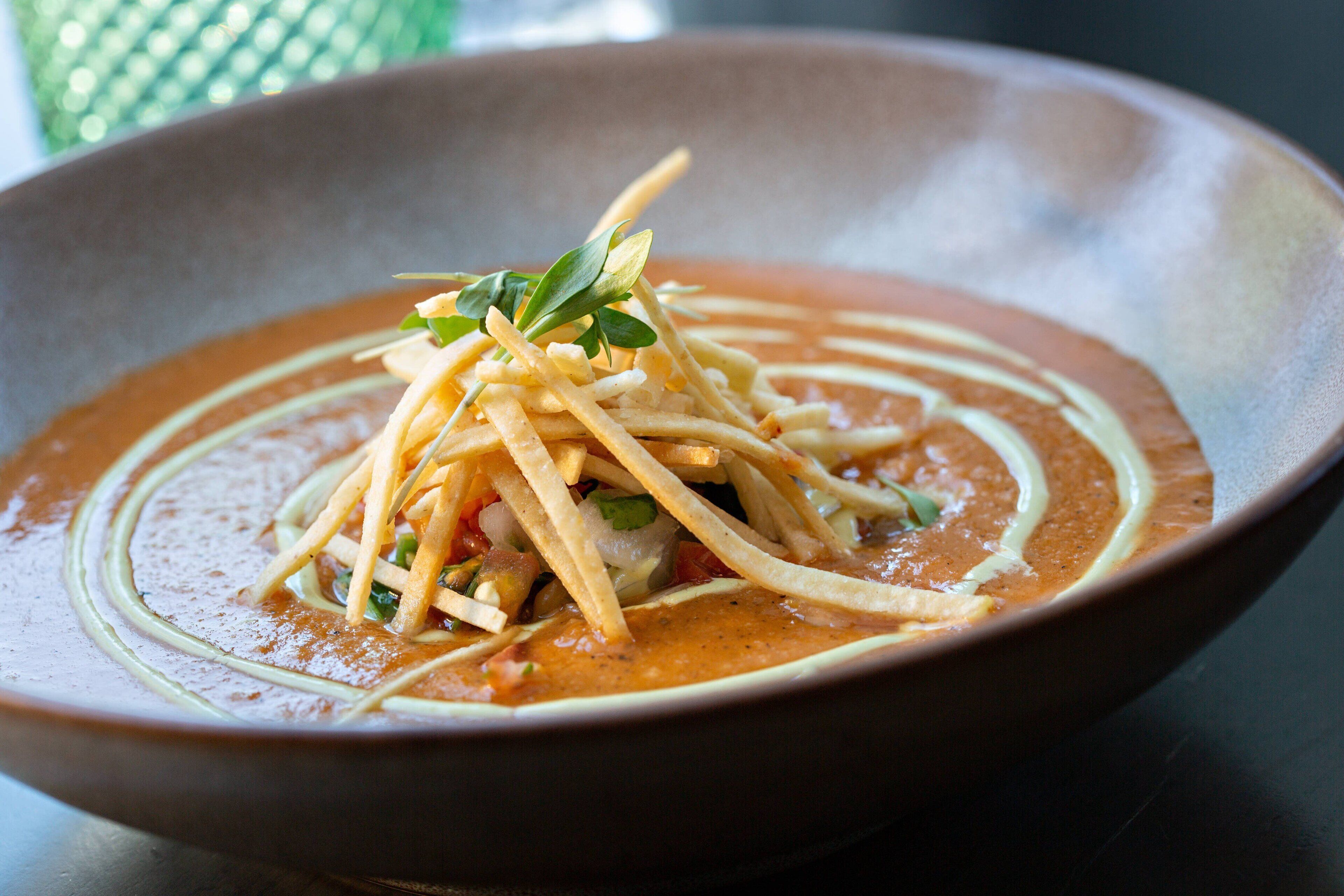A bowl of soup with a creamy base and garnished with thin strips and green leaves.