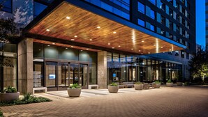 A modern hotel entrance with a wooden ceiling, large windows, and outdoor seating area. - Houston Cityplace Marriott at Springwoods Village (Spring)