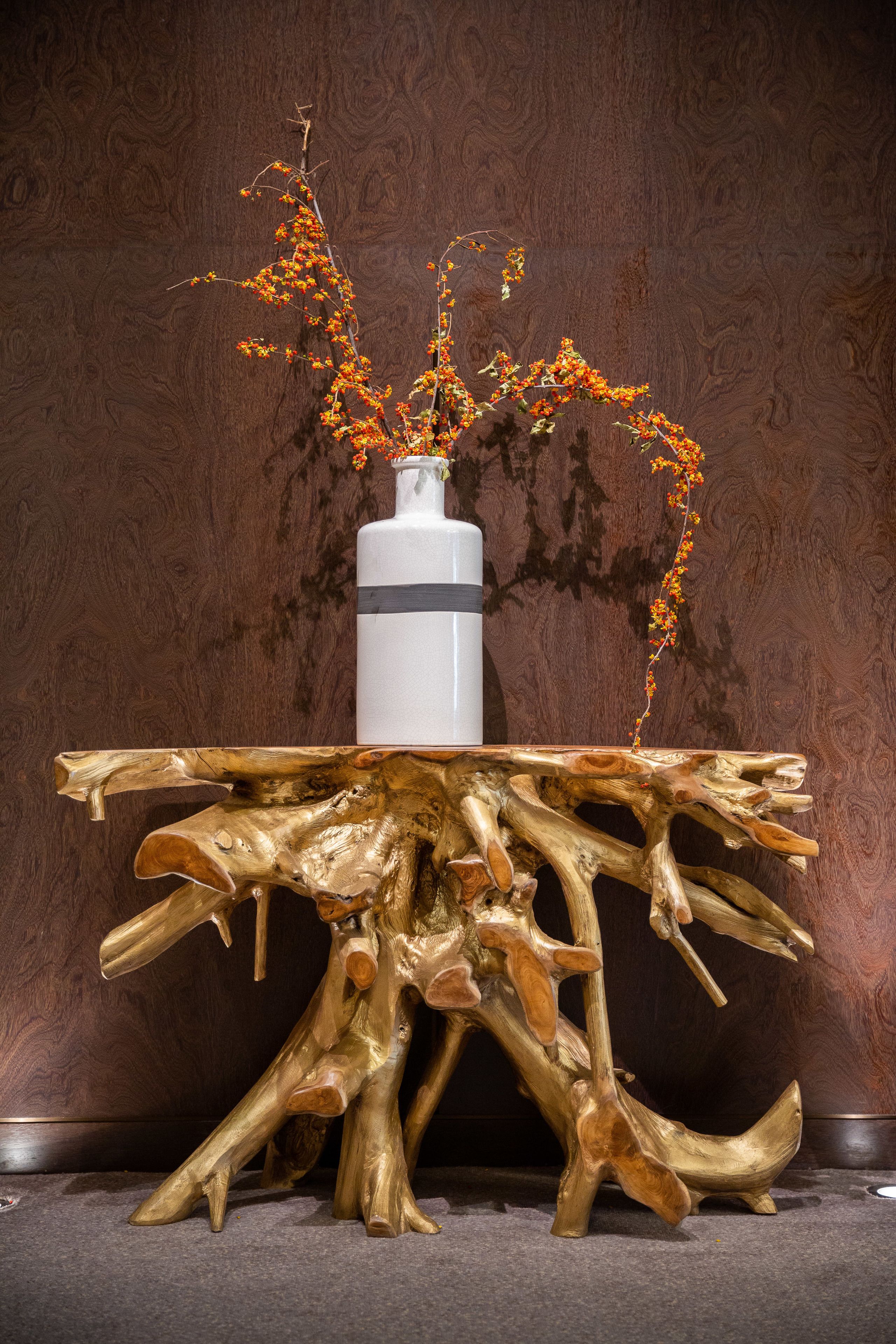 A table with a unique wooden design and a vase with orange flowers.