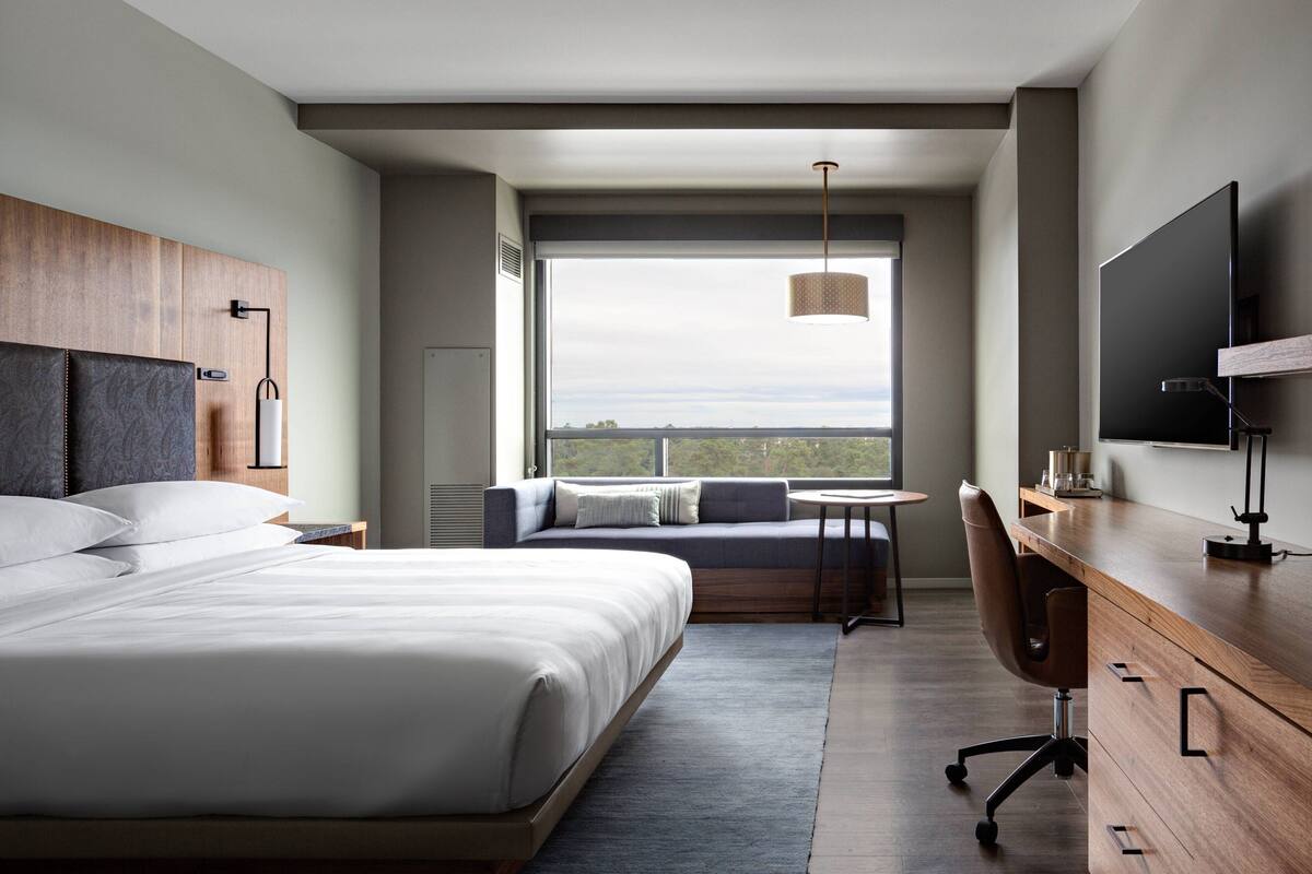 A modern hotel room with a large bed, a desk, a sofa, and a TV.