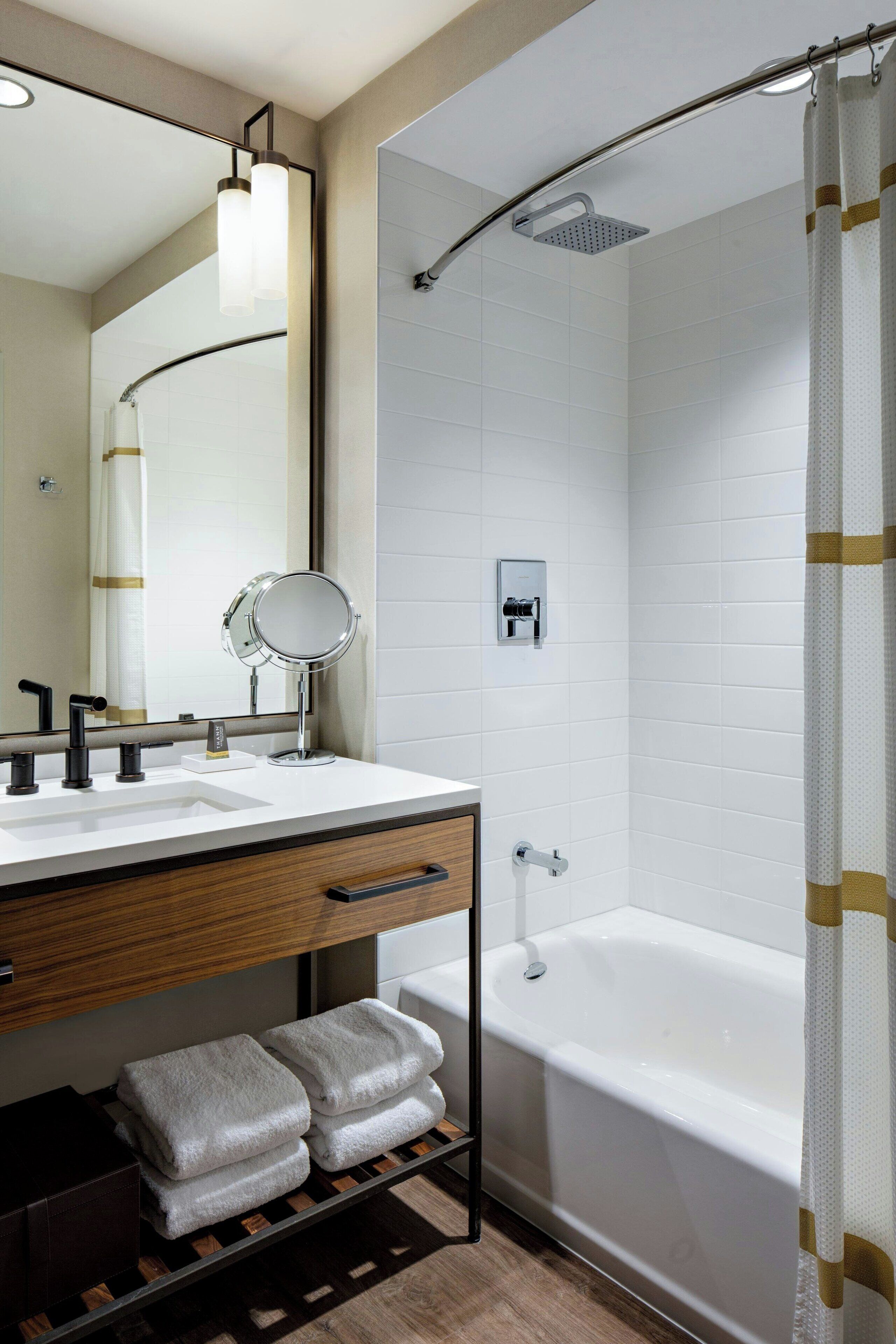 A modern bathroom with a white bathtub, a shower with a curved glass door, a vanity with a mirror, and a towel rack.
