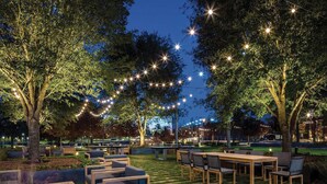 An outdoor seating area with tables and chairs, surrounded by trees and string lights. - Houston Cityplace Marriott at Springwoods Village (Spring)