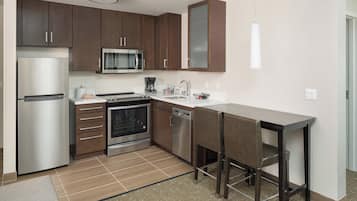 A modern kitchen with stainless steel appliances, wooden cabinets, and a bar area with stools.