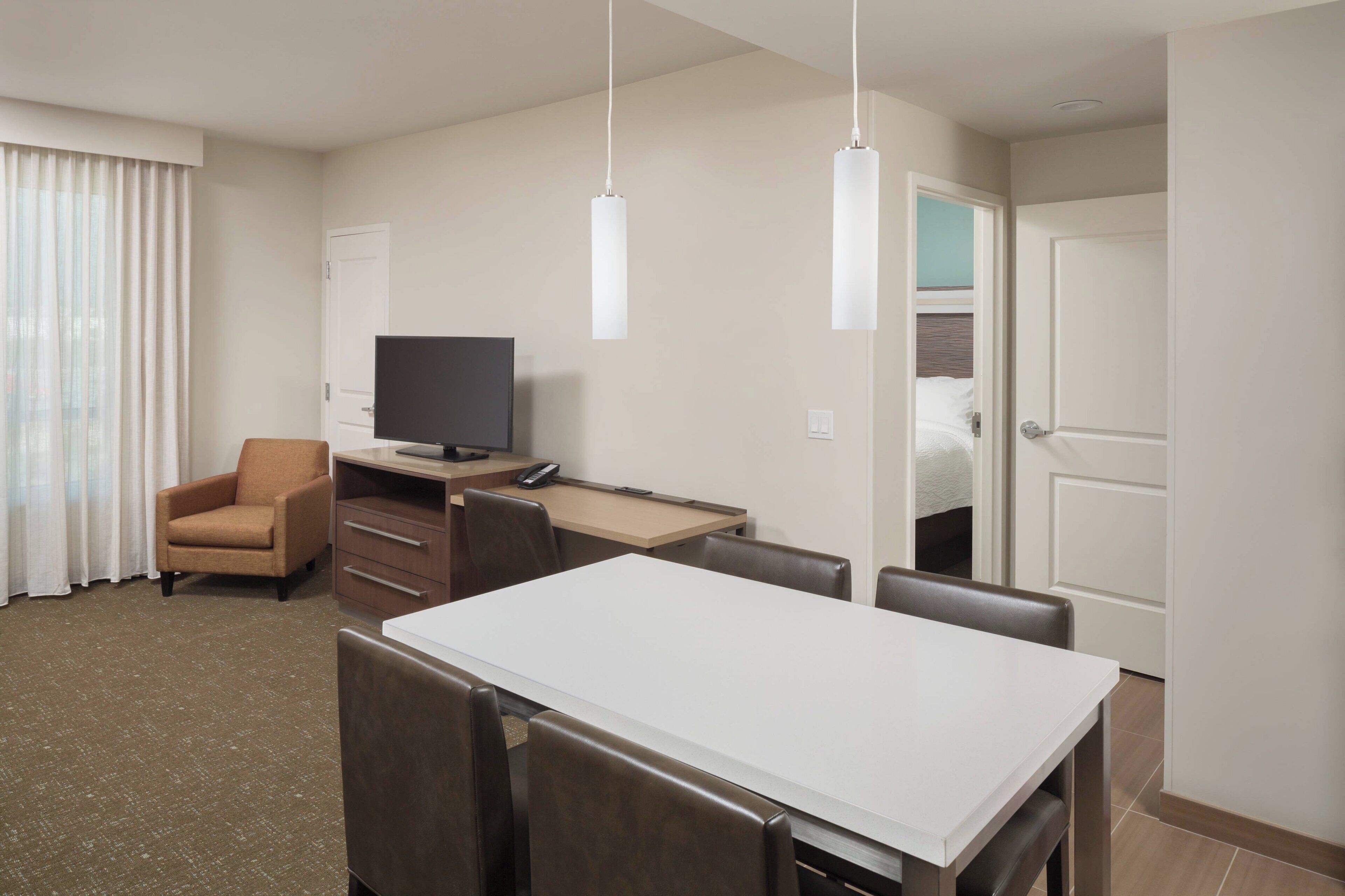 Una habitación de hotel con cama, escritorio, computadora, silla, televisor y mesa de comedor.