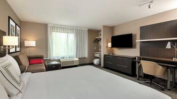 A hotel room with a large bed, a desk, a chair, a TV, and a window with curtains.