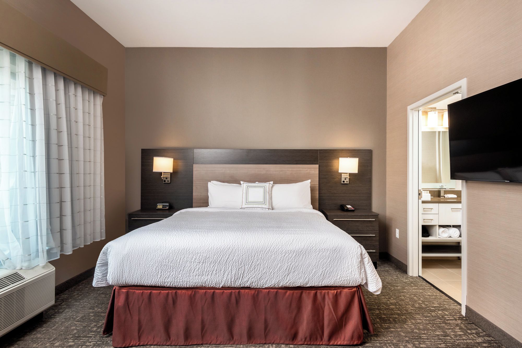 A hotel room with a large bed, bedside lamps, a TV, and a walk-in closet.