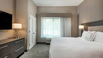 A hotel room with a large bed, a flat-screen TV, a dresser, and a window with sheer curtains.