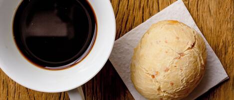 A white cup of coffee on a wooden table next to a pastry on a napkin.
