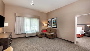 A hotel room with a sofa, a desk, a chair, a bed, a TV, and framed pictures on the wall.
