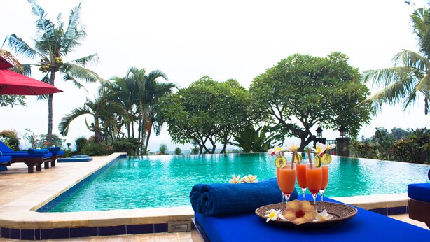 A poolside area with a blue lounge chair, a red umbrella, and a table with drinks and a flower arrangement. - Ume Cantik Villa (Sukasada)