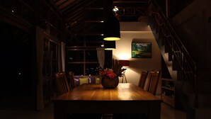 A dining area with a wooden table, chairs, and a vase with flowers. There is a staircase and a painting on the wall. - Ume Cantik Villa (Sukasada)