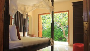 A bedroom with a bed, a red bean bag, a wooden door, and a view of greenery outside. - Ume Cantik Villa (Sukasada)
