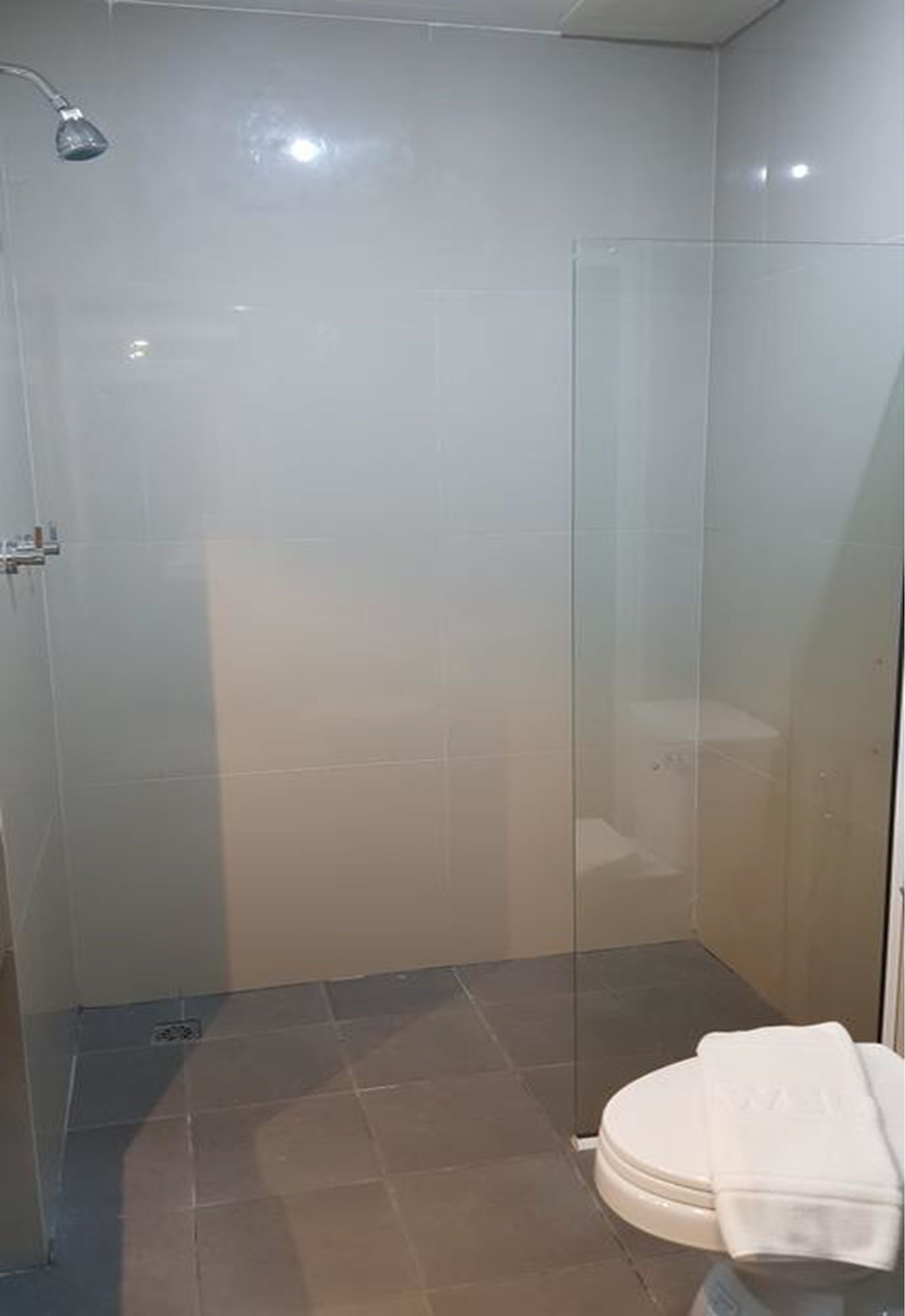 Eine begehbare Dusche mit Glaswänden, eine weiße Toilette und ein Handtuch auf dem Sitz.