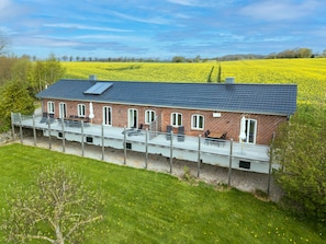 A brick house with a balcony overlooking a field of yellow flowers. - Remise II - Apartments Gut Ostergaard (Steinberg)