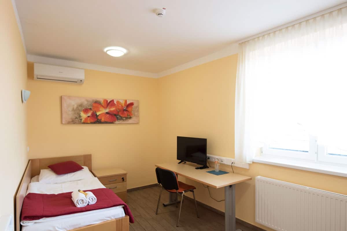 A bedroom with a bed, desk, chair, and a painting on the wall.