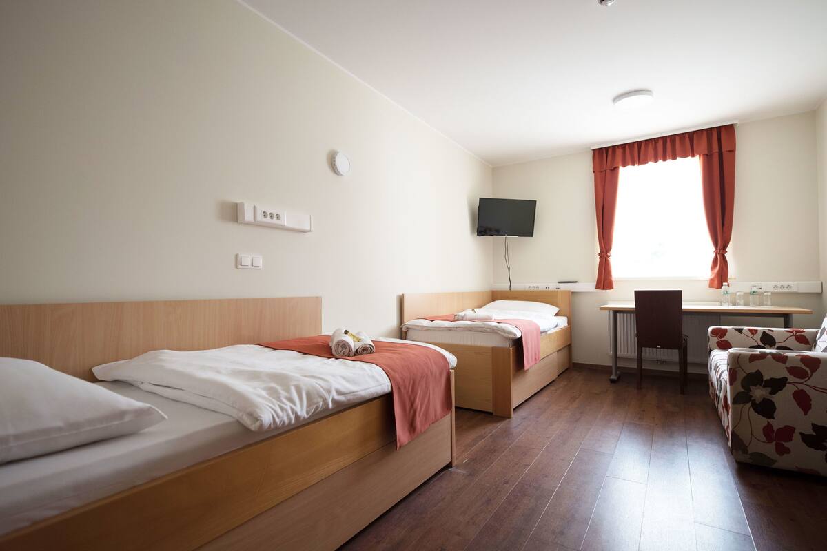 A hotel room with two single beds, a desk, a chair, and a TV on the wall.