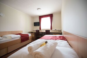 A hotel room with two single beds, a desk, a chair, a TV, and a window with curtains. - S hotel (Maribor)