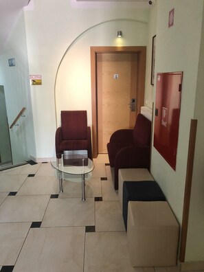A lobby with a glass table, two red armchairs, a wooden door, and a red cabinet. - S hotel (Maribor)