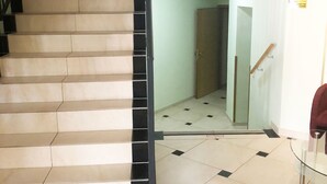 Una escalera con barandillas negras y baldosas color crema que lleva a una habitación con una puerta y un cartel con forma de señal de stop.