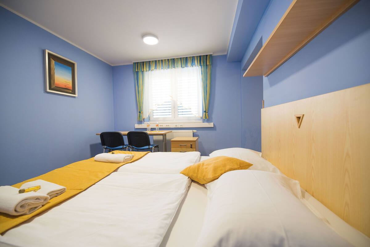 A hotel room with two beds, a desk, a chair, and a window with curtains.