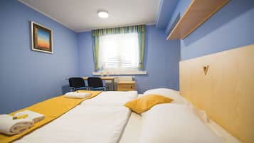 Une chambre d’hôtel avec deux lits, un bureau, une chaise et une fenêtre avec des rideaux.
