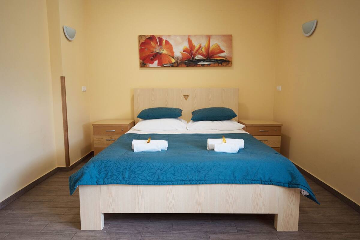 A neatly made bed with a blue bedspread, two pillows, and two towels.