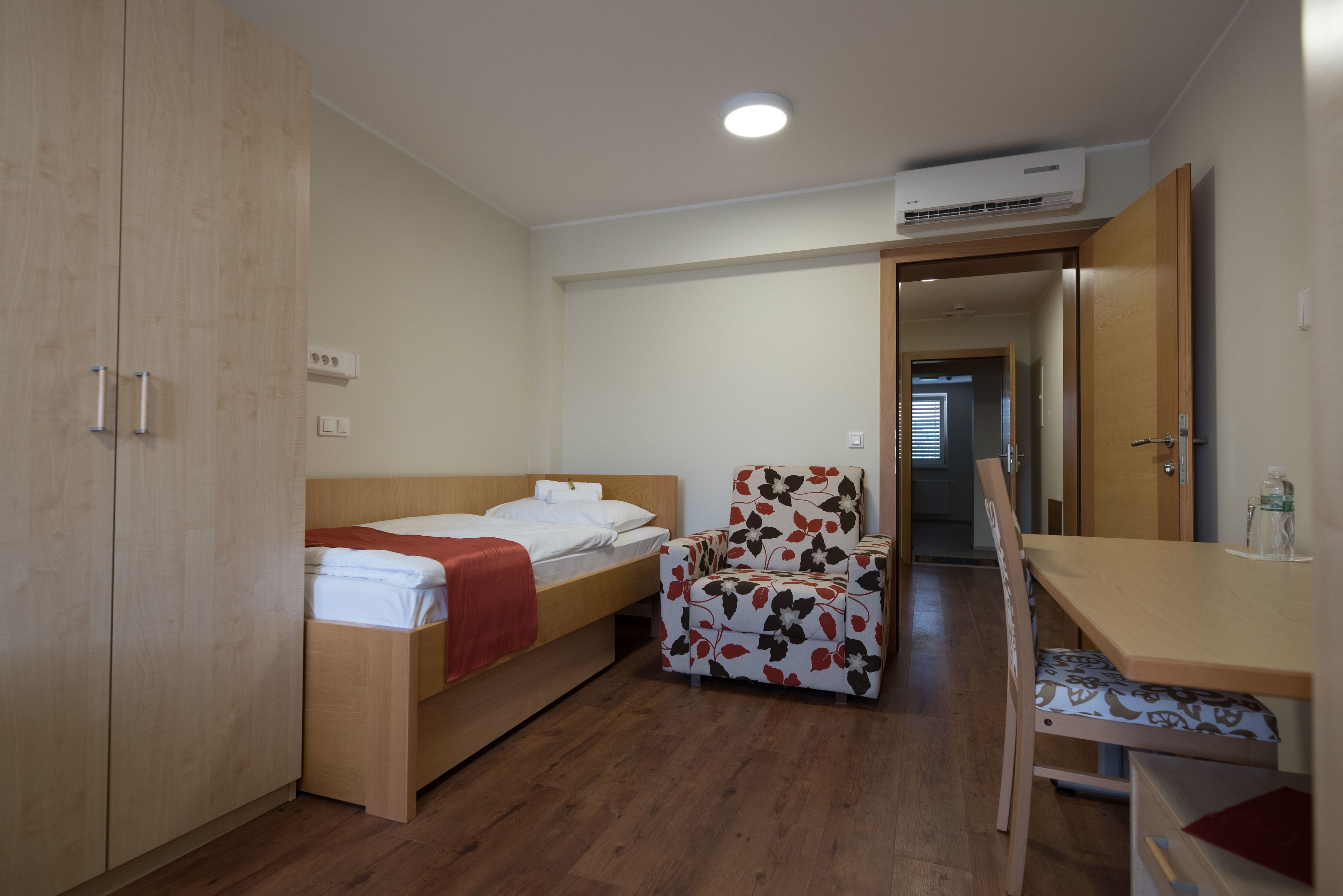 Um quarto com cama, cadeira, escrivaninha e guarda-roupa.