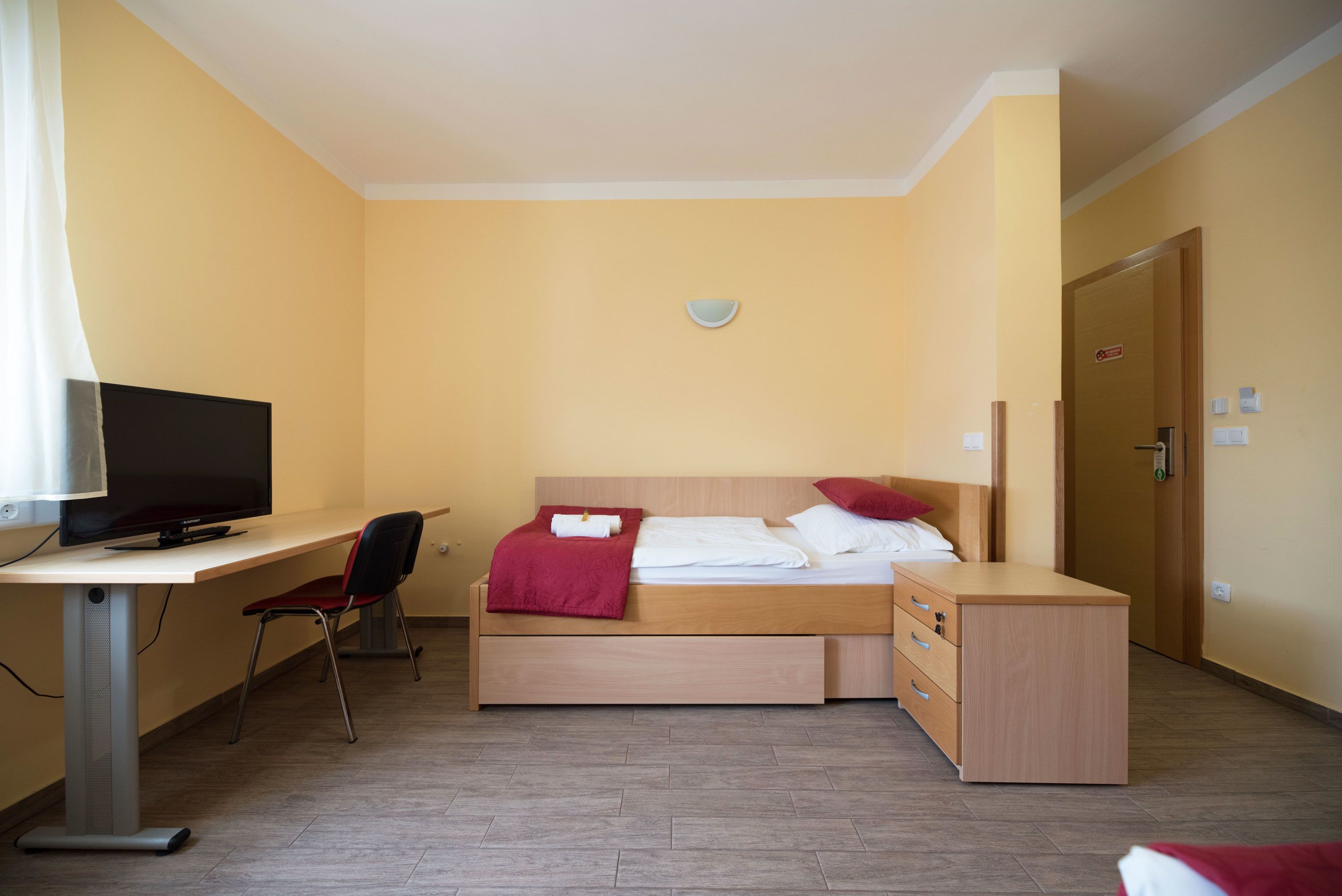 Una habitación de hotel con cama, escritorio y televisor, además de una silla.