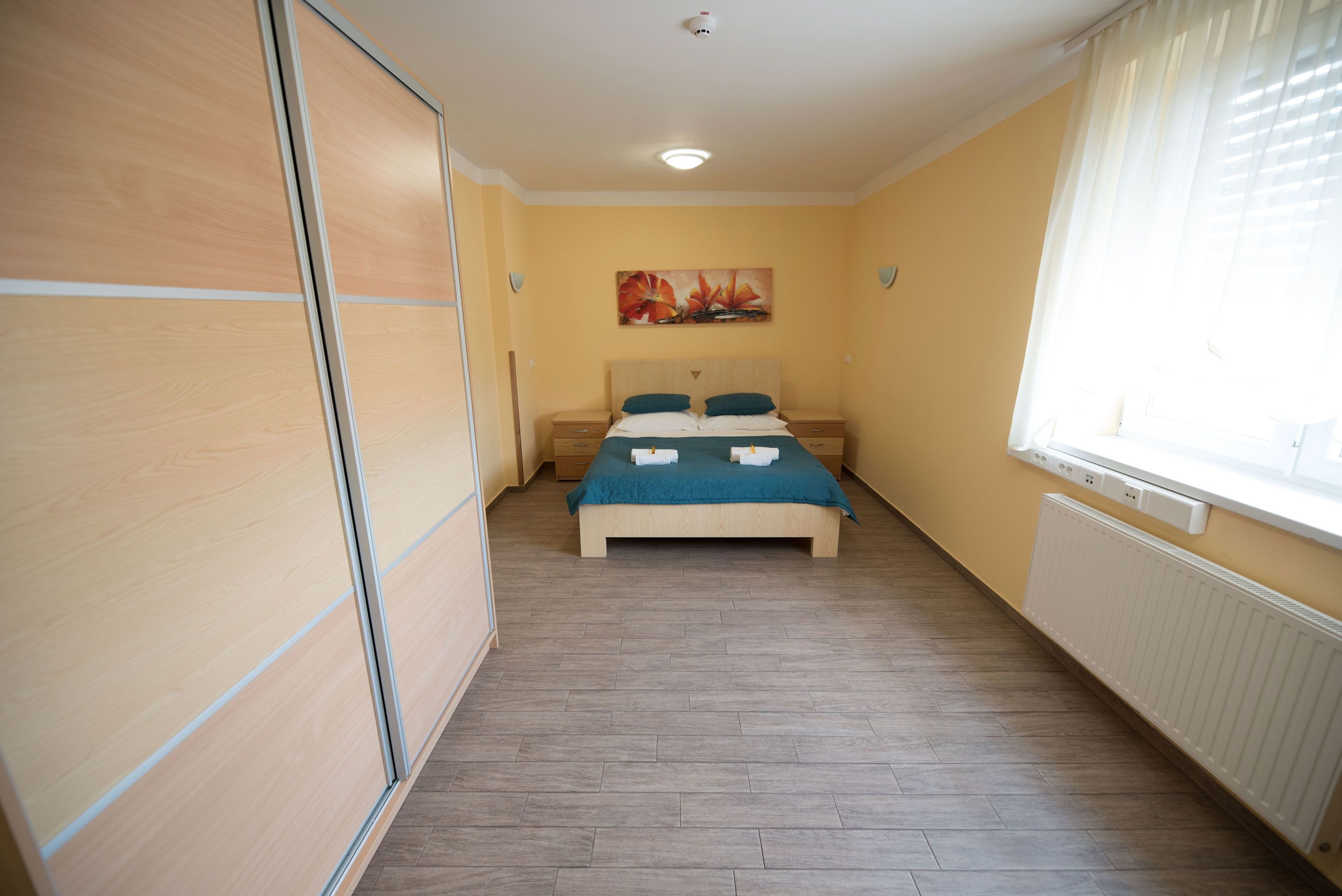 A bedroom with a bed, wooden wardrobe, and a painting on the wall.