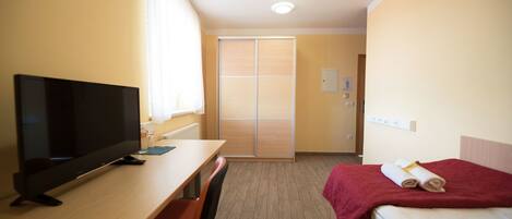 A hotel room with a TV, a desk, a chair, a bed with a red blanket, and a sliding door closet.