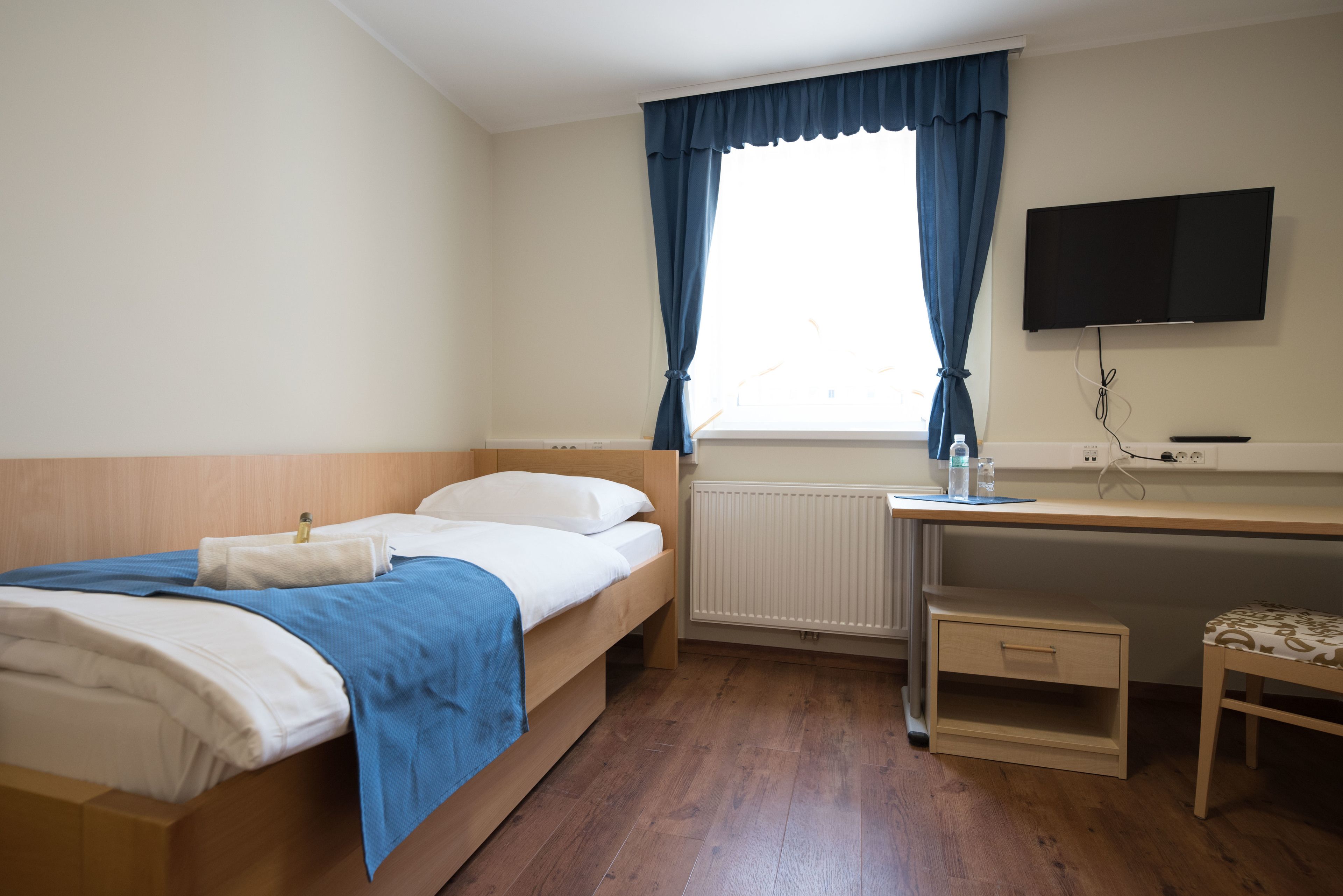 Un dormitorio con cama, escritorio, silla, televisor y ventana con cortinas.