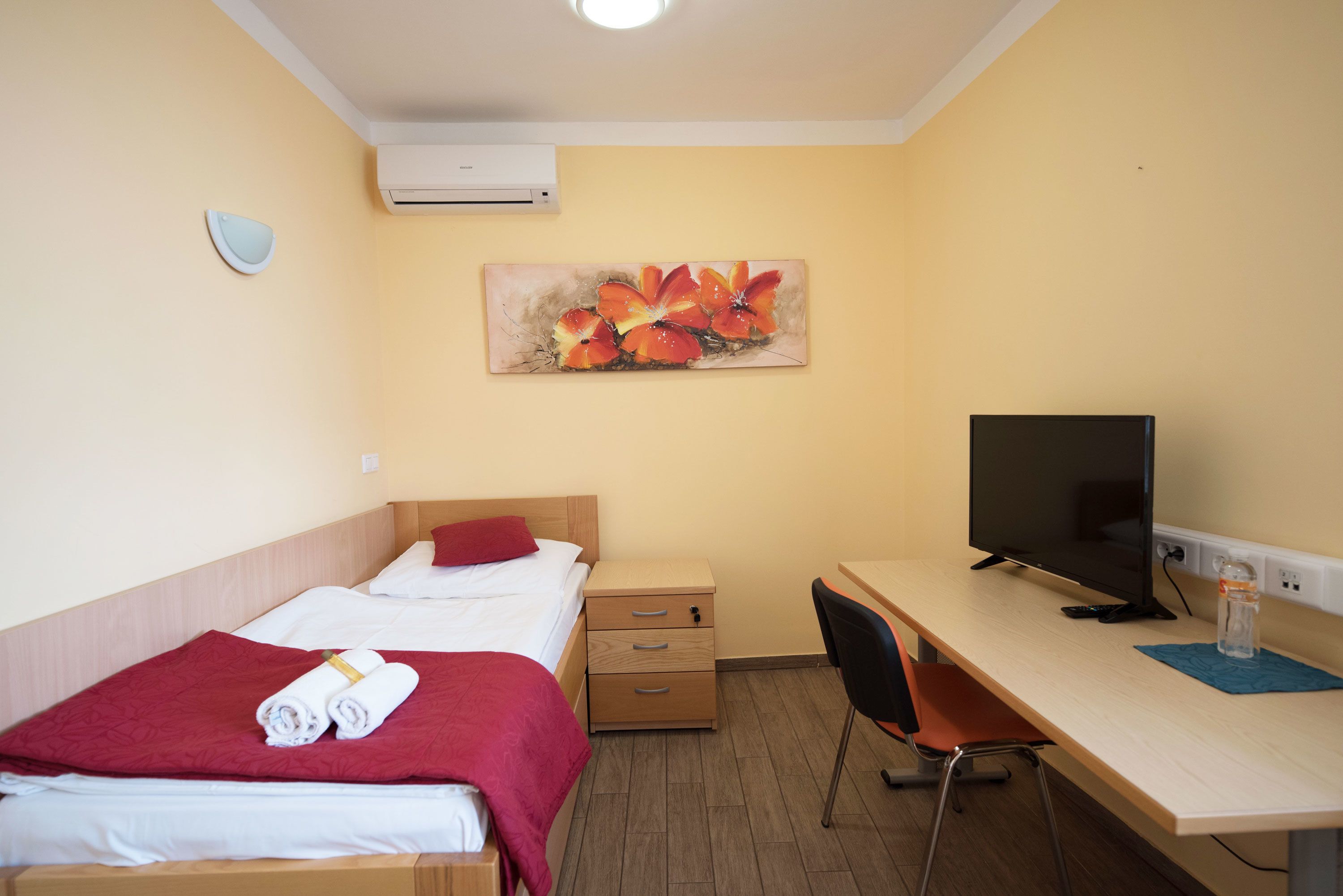 A hotel room with two beds, a desk with a computer, a chair, and a wall-mounted air conditioner.