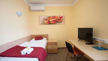 A hotel room with two beds, a desk with a computer, a chair, and a wall-mounted air conditioner.