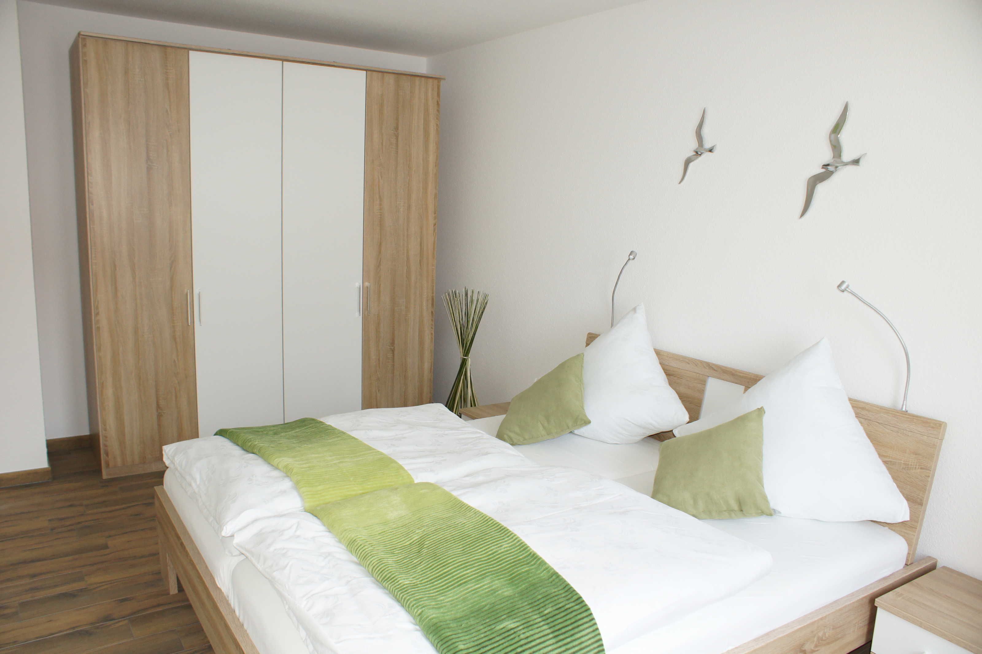 Ein Schlafzimmer mit einem Bett, einem Holzschrank und Wandschmuck in Form von Vogelbildern.