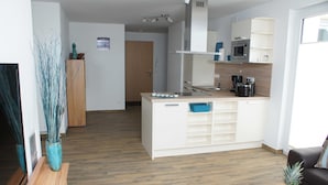 A modern kitchen with white cabinetry, a microwave, and a coffee maker. There is a wooden floor and a blue rug in the living area. - Störtebeker Suite, Germany (Glowe)