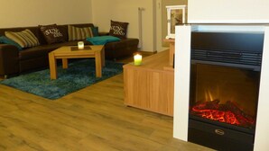 A living room with a sofa, a coffee table, a fireplace, and a wall-mounted welcome sign. - Störtebeker Suite, Germany (Glowe)