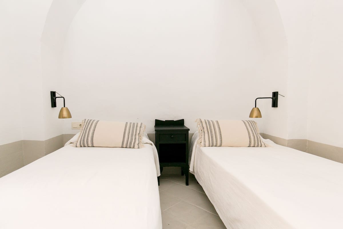 A twin room with two single beds, a small table, and two wall-mounted lamps.