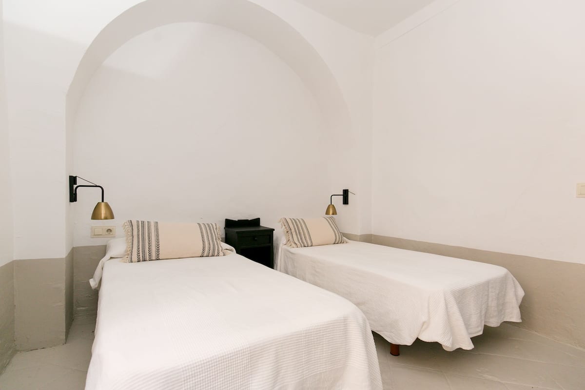 A room with two single beds, a black nightstand, and two wall-mounted lamps.