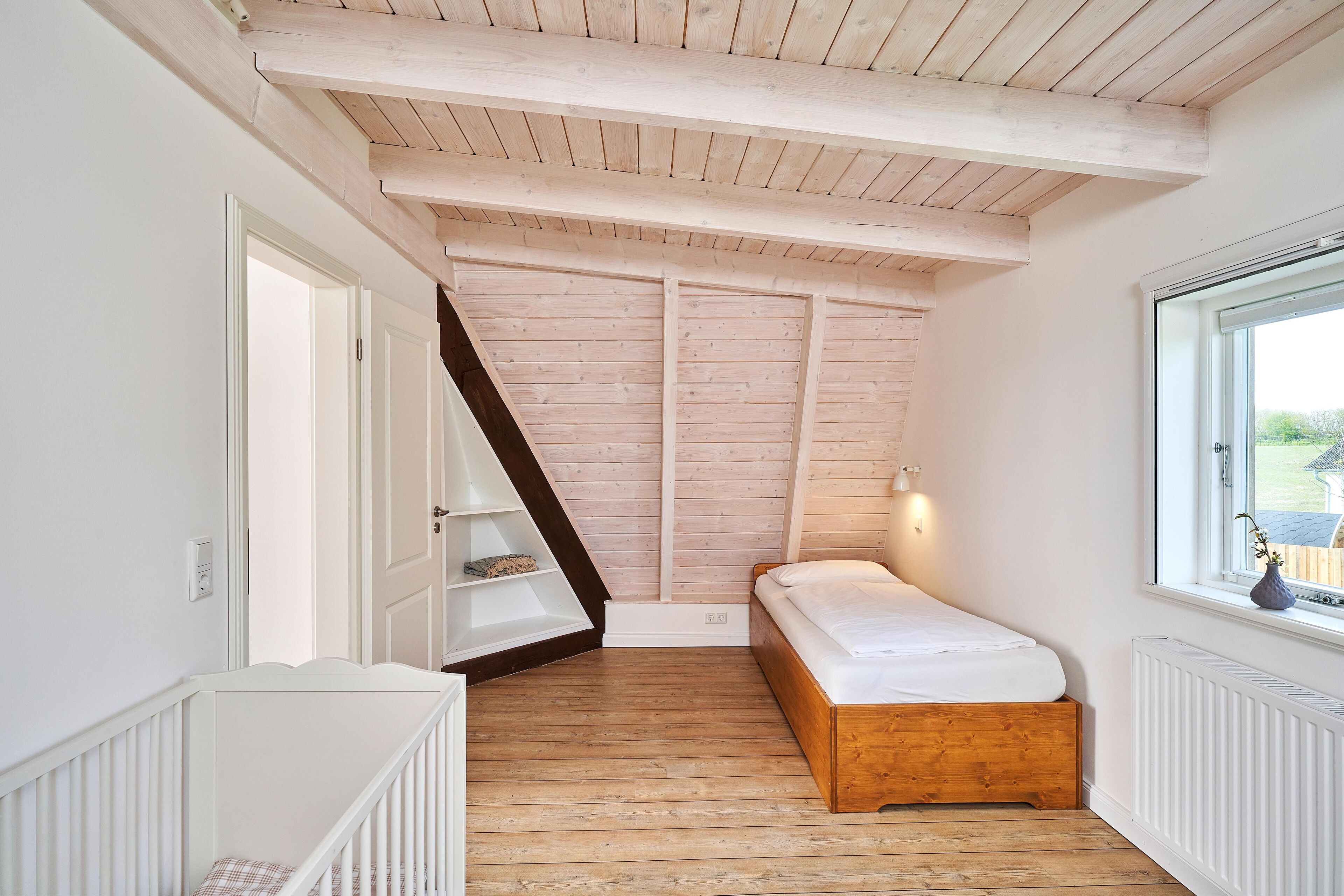 A bedroom with a sloped ceiling, a wooden bed, a white radiator, and a window with a view of the outside.