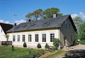 Een woonhuis met twee verdiepingen, een schuin dak, veel ramen en een kleine tuin met stenen en planten.